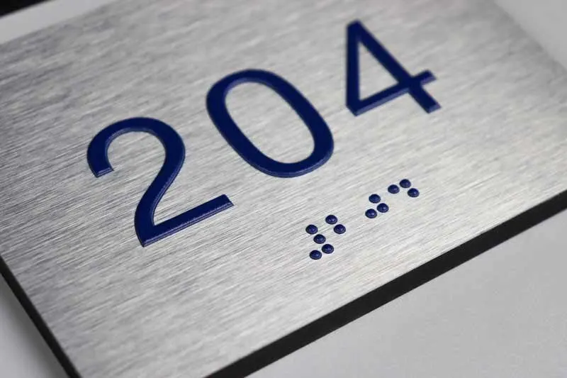 Brushed aluminum plate with raised numerals and Grade 2 braille.